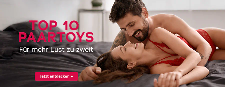 Ein Paar, welches sich anlächelt, liegt auf einem Bett mit dunkler Decke. Die Frau trägt rote Spitzenunterwäsche, der Mann liegt halb über ihr und umarmt sie. Grossflächig steht der Text „Top 10 Paartoys – Für mehr Lust zu zweit“. Unten roter Button mit weisser Schrift „Jetzt entdecken ».