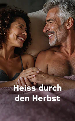 Ein Paar liegt dicht zusammen im Bett und lächelt sich an. Links eine Frau im Spitzen-BH und dunklen Locken, rechts ein oberkörperfreier Mann, mit grauem Haar und Bart. Text: „Heiß durch den Herbst.“ Roter Button: „Entdeckt Lust-Booster."